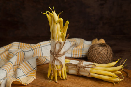 Cutting board with two bunch of raw yellow pods of haricot and yellow kitchen towel on wooden background. French beans or Green beans also known as String beans from India. Vegetables collection.の写真素材