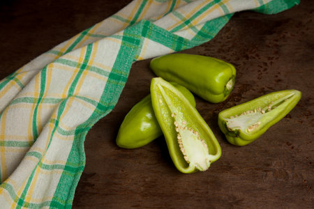 Two whole and halves of green bell pepper (capsicum) known as sweet bell pepper, paprika with green kitchen towel on vintage wooden background. Vegetables collection.の写真素材