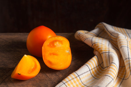 Cut and whole of ripe juicy yellow tomato and yellow towel on vintage wooden background. Vegetables collection.の写真素材