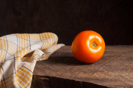 Whole ripe juicy yellow tomato with yellow towel on wooden background. Vegetables collection.の写真素材