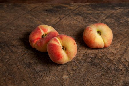 Three ripe chinese flat peach fruits or saturn peaches on vintage wooden background.の写真素材