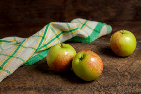 Three fresh green apples on wooden background with green kitchen towel.の写真素材