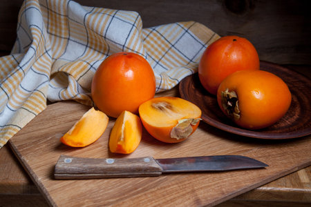 Composition of ripe delicious whole persimmon fruits, half and sliced fruit ready for eat with vintage knife on wooden background.の写真素材