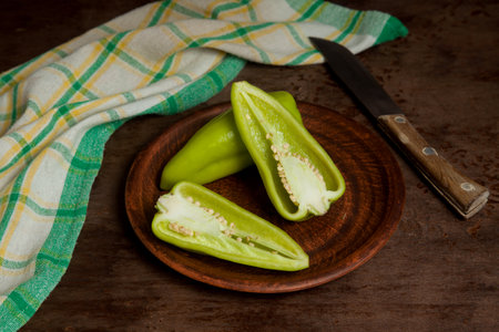 Clay plate with whole and halves of green bell pepper (capsicum) known as sweet bell pepper, paprika and green kitchen towel on vintage wooden background. Vegetables collection.の写真素材