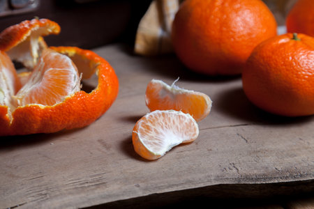 Several of unpeeled whole fresh orange mandarine or oranges, tangerines, clementines, citrus fruits, one fruit is half peeled and slices of peeled mandarin on wooden boardの写真素材