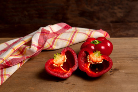 Whole and halves of red bell pepper (capsicum) known as sweet bell pepper, paprika on vintage wooden background with red kitchen towel.の写真素材