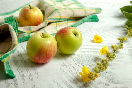 Three fresh green apples on white wooden background with green kitchen towel.の写真素材