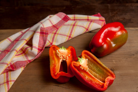 Whole and half red bell pepper (capsicum) known as sweet bell pepper, paprika on vintage wooden background with red kitchen towel.の写真素材