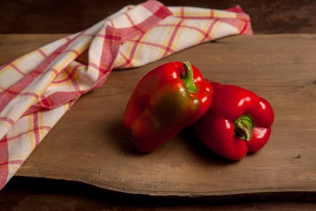 Two whole red bell pepper (capsicum) known as sweet bell pepper, paprika on vintage wooden background with red kitchen towel.の写真素材