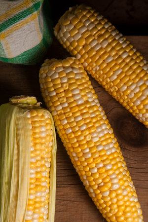 Close up view of three ears of ripe sweet corn with green leaves and green towel on vintage wooden...