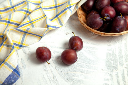 Juicy summer plum fruit. Several ripe sweet plums on white wooden background with blue kitchen towel.の写真素材