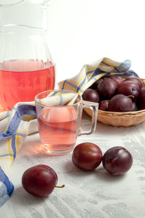 Plum Compote in jug and cup with several ripe sweet plums on white wooden background with blue kitchen towel. Juicy summer plum fruit.の写真素材