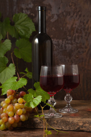 The concept of a delicious alcoholic drink, wine and grapes. Wine bottle, glasses of red wine and bunch of grapes on dark rustic wooden background with grapes leaves.の写真素材