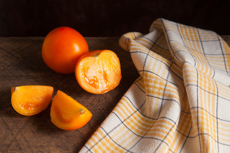 Cut and whole of ripe juicy yellow tomato and yellow towel on vintage wooden background. Vegetables collection.の写真素材