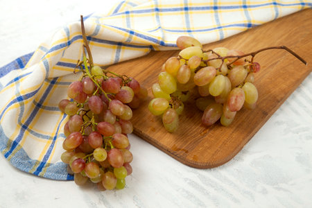 Cutting board with big bunch of ripe pink grapes on white. Pink wine grapes with blue kitchen towel on white wooden background.の写真素材