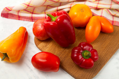 Wooden cutting board with several whole ripe red and yellow tomatoes and bell pepper on white wooden background with red kitchen towel. Vegetables collection.の写真素材