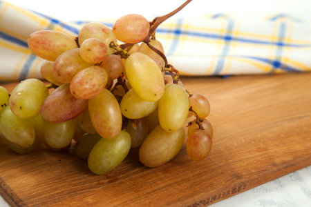 Cutting board with big bunch of ripe pink grapes on white. Pink wine grapes with blue kitchen towel on white wooden background.の写真素材