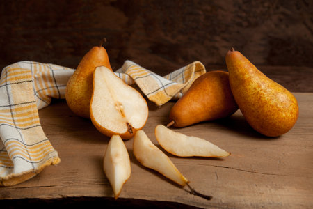 Whole, half and slices of ripe juicy pear fruits on vintage wooden background with yellow kitchen towel.の写真素材