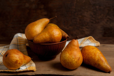 Several whole ripe juicy pear fruits and clay bowl with pears on vintage wooden background with yellow kitchen towel.の写真素材