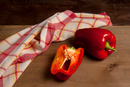 Whole and half red bell pepper (capsicum) known as sweet bell pepper, paprika on vintage wooden background with red kitchen towel.の写真素材
