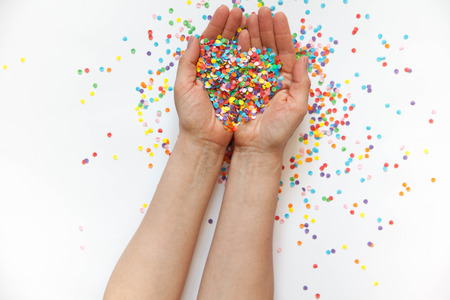 Hands holding festive confetti. White background. Small circles of colored paper. Heart made of colored confetti.の写真素材