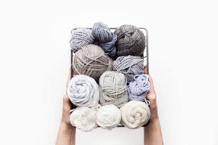Female hands hold a black metal basket with yarn for knitting gray and white.の写真素材