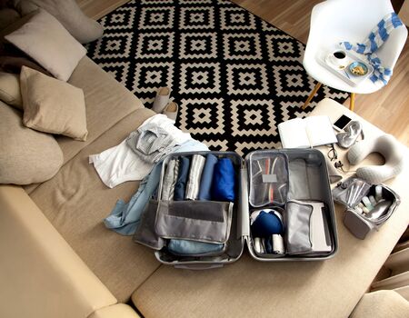 Female hands packing traveler case on bed, closeup. Beach accessories in opened suitcase. Travelling...