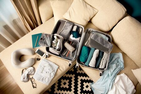 Female hands packing traveler case on bed, closeup. Beach accessories in opened suitcase. Travelling...