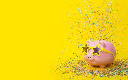 Pink piggy bank with birthday color confetti on yellow background.の写真素材