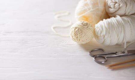White and beige knitting wool and knitting needles on white wooden background.