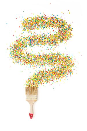 A paint brush draws a line wave of colored festive confetti. White background.の写真素材