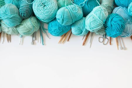 Yarn of green, turquoise, aquamarine and blue colors. White wood background. Knitting needles and...