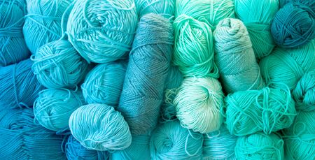 Yarn of green, turquoise, aquamarine and blue colors. White wood background. Knitting needles and crochet hooks. Scissors. White background.の写真素材