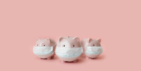 Three piggy banks with medical masks stand on pale pink backgroundの写真素材