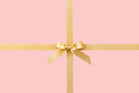 Gold ribbon with a bow as a gift on a pink backgroundの写真素材