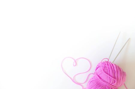 A skein of pink yarn and a frame in the shape of a heart. Colored yarn and knitting needles. White background.の写真素材