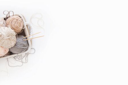 Neutral beige yarn for knitting is in the basket. Knitting needles, scissors. White background.の写真素材