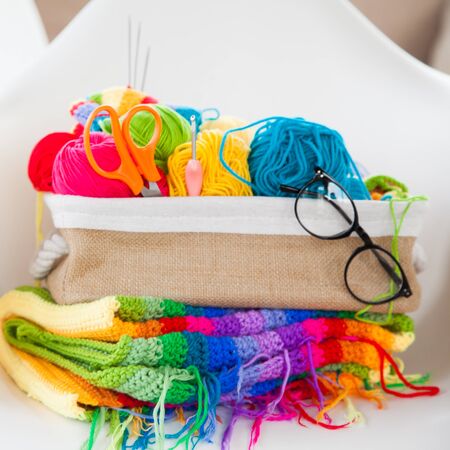 Basket with colored, bright yarn for knitting on a white armchair. Crochet.