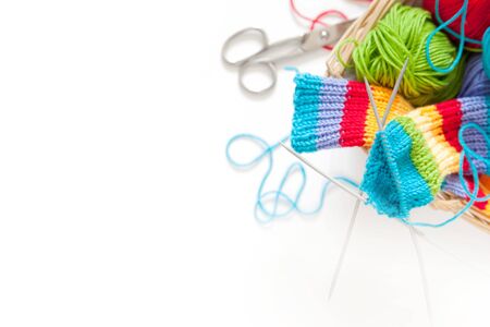 Knitting for children. Bright striped rainbow socks. Colored yarn. White background. Wicker basket.