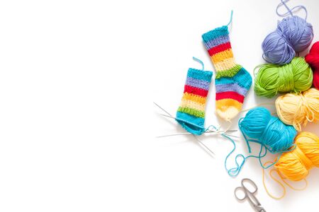 Knitting for children. Bright striped rainbow socks. Colored yarn. White background.