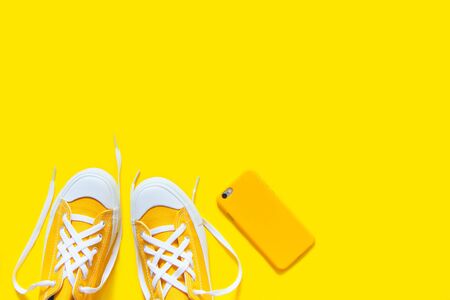 Short low bright sneakers on a yellow background. Mobile phone in a yellow case and earphonesの写真素材