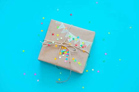 Craft broun gift box. Drawing of a colored garland, flags. Blue and turquoise background. Confetti.の写真素材