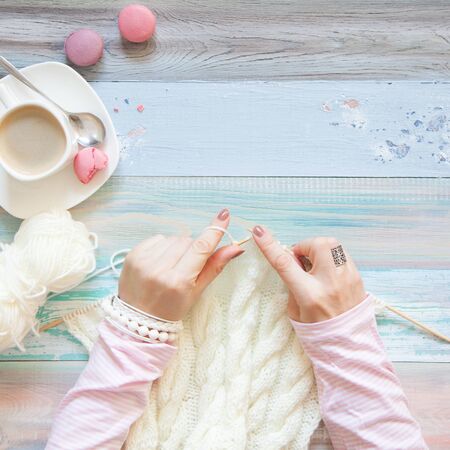 Knitting with knitting needles. White knitted fabric. Coffee Americano. Light aged background.