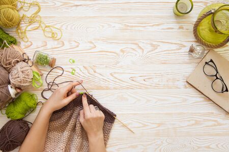 A woman knits a white and broun knitted fabric of woolen yarn. Knitting needles. Aged background. Green and white.の写真素材