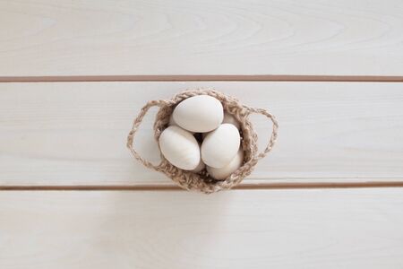 Wooden Easter eggs in a wicker, knitted basket. White wood background.の写真素材