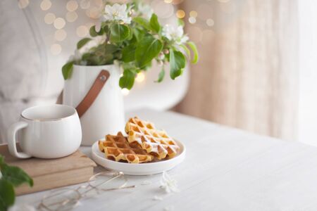 A bouquet of branches of a blossoming apple tree stands in a white vase on the table. Viennese...