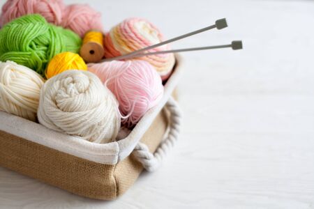 Woolen and cotton bright yarn lies in a basket. Glasses lie on a white wooden background.