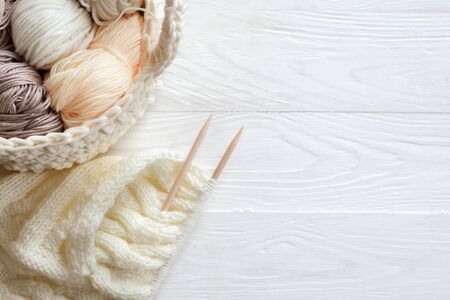 The beginning of the knitting process. Knitting needles. Basket with skeins of wool and cotton yarn. White wood background.の写真素材