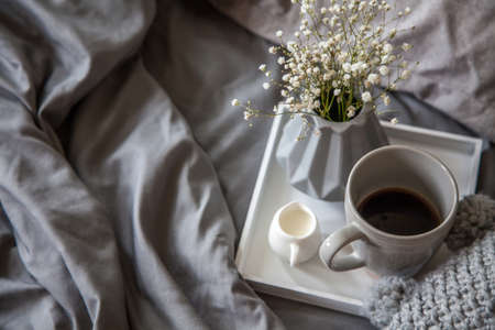 Morning breakfast in bed. Gray bedding. Golden tray in the nordic style. White cup with black coffee and a milkman with milk. Flowers in a gray vase.の写真素材