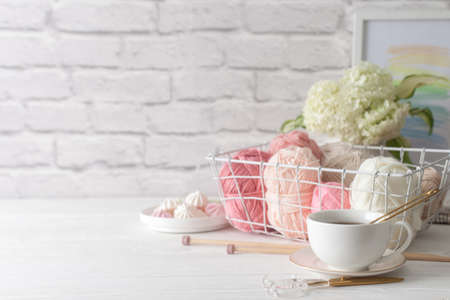 Needlework accessories in a white metal basket. Pink yarn. Gray and wooden knitting needles. White...